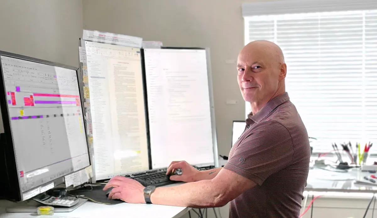 S. A. Weigle at computer workstation, looking over shoulder while writing with multiple monitors