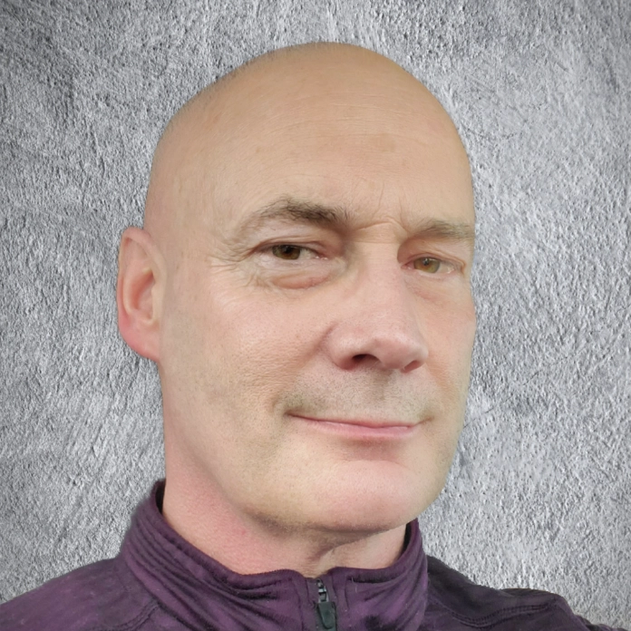 S. A. Weigle headshot against gray wall, looking at camera with slight smile