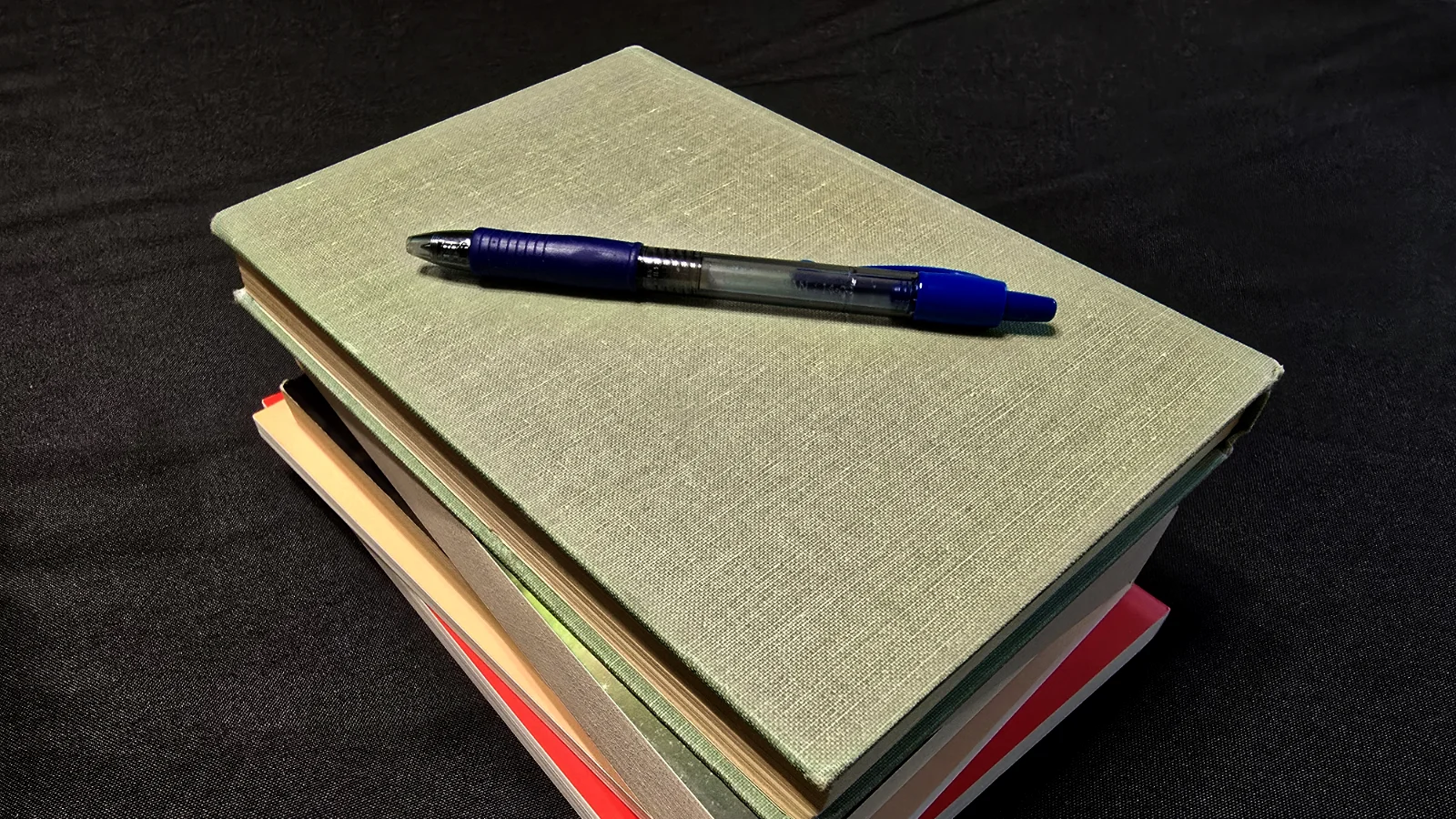 Short stack of books with blue pen resting on top on black tablecloth