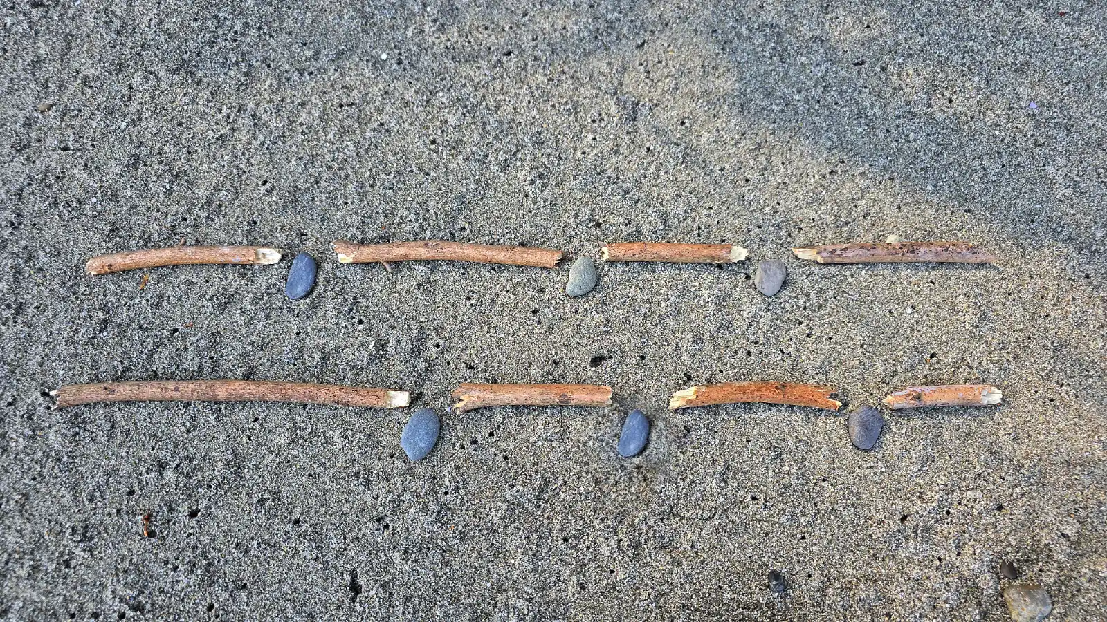 Pieces of sticks representing text in two lines on a beach with pebbles serving as commas